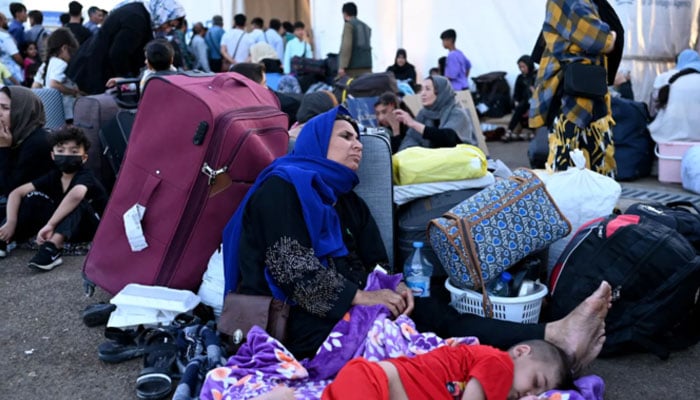 Afghan refugees rest with their belongings after arriving at the zero point of the Islam Qala border crossing between Afghanistan and Iran, following their deportation from Iran. — AFP/File