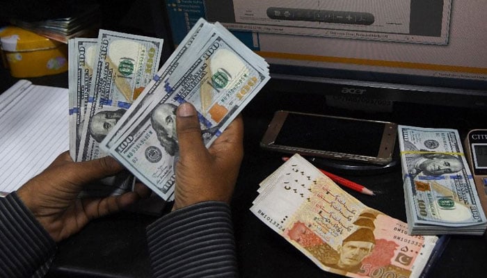 A dealer counts US dollars at a currency exchange shop in Karachi, Pakistan. —AFP/File
